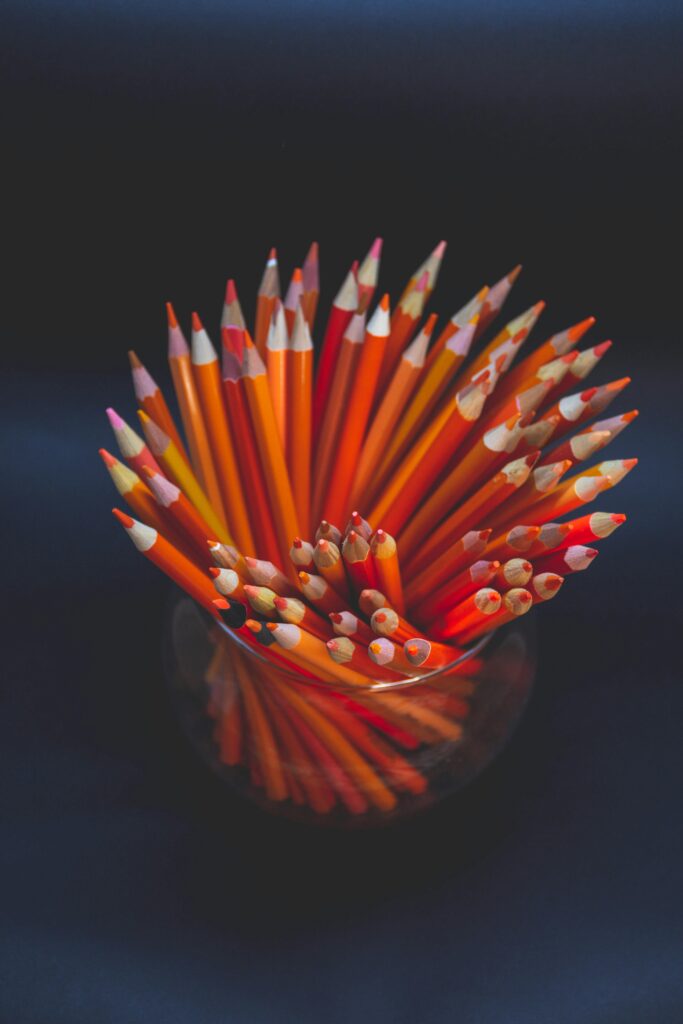 Top view of vibrant orange pencils arranged in a glass container against a dark background.